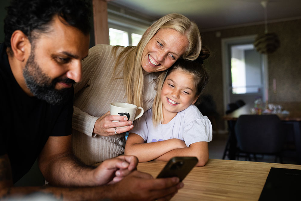 a father, mother and daughter looking and smiling at a mobile phone screen