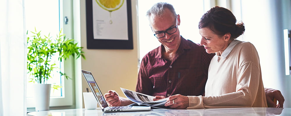 An elderly couple looking at documents and a laptop in a bright kitchen
