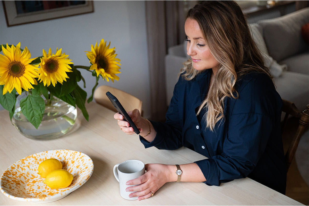 A woman sitting at a table using her phone, with sunflowers and lemons nearby.