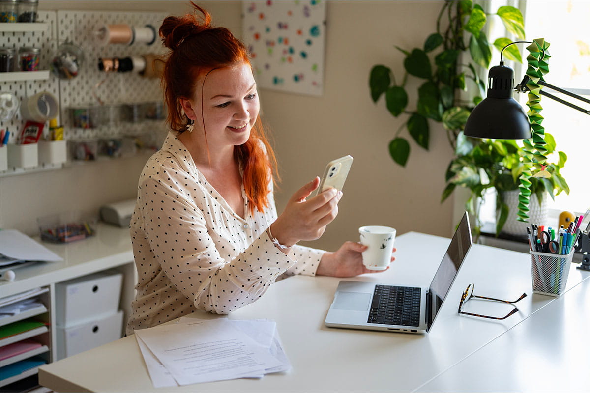 A person working at a desk with a phone, laptop, and coffee cup.