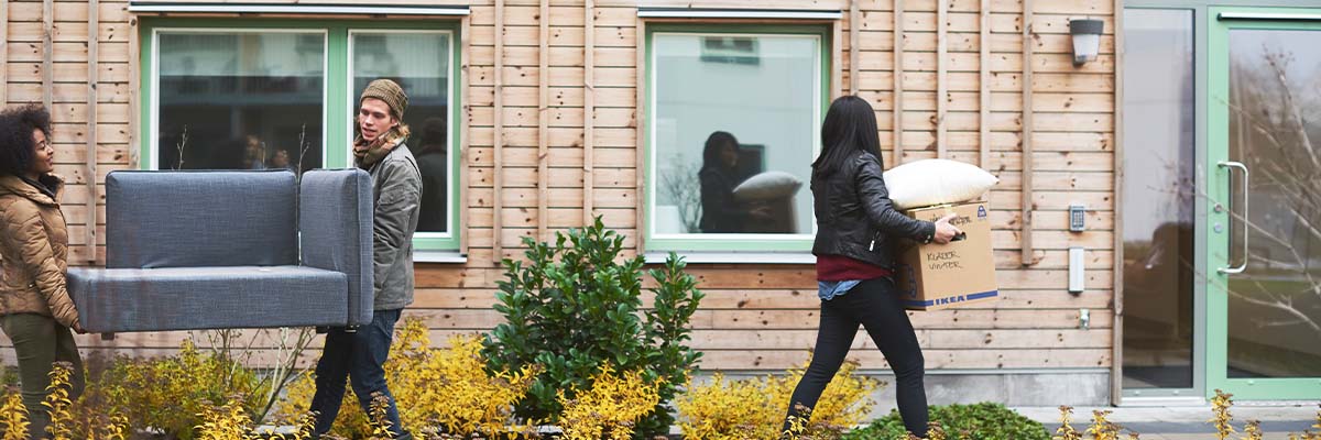 Three people moving boxes and furniture into an apartment block
