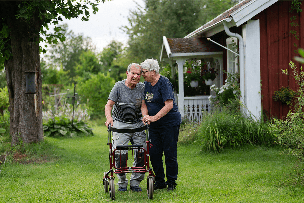 Elderly couple walking through a green garden outside a red wooden house