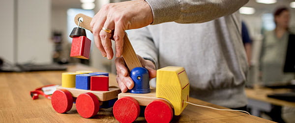 A person using a wooden toy crane truck on a table.
