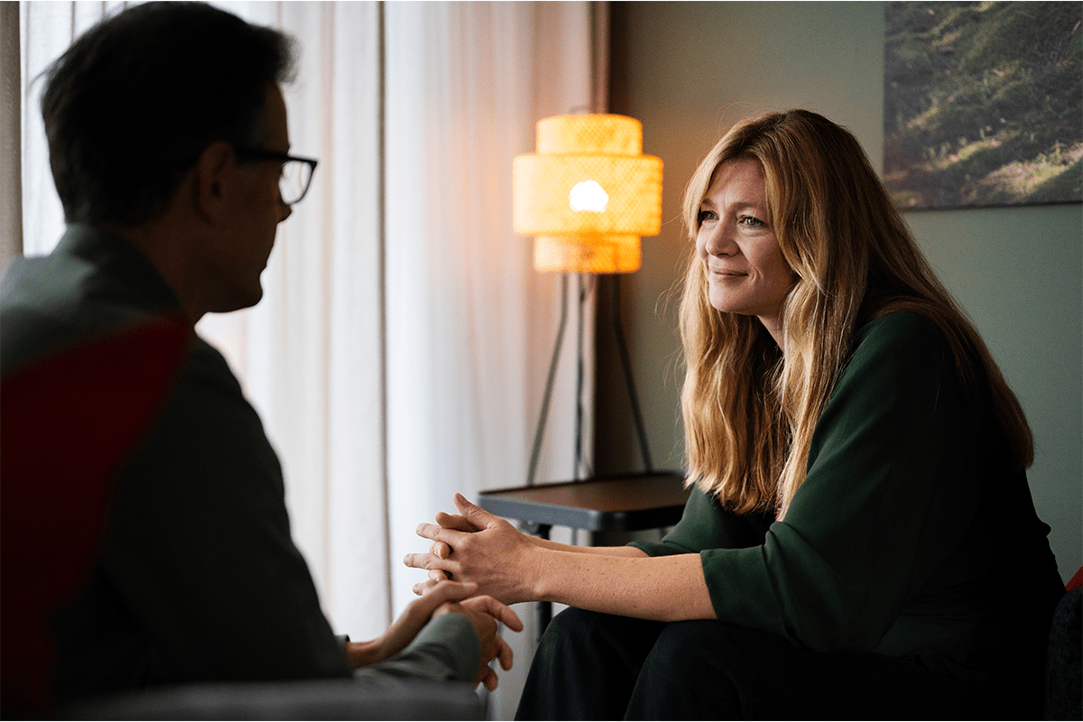 Woman sitting and talking with a man in a calm indoor setting, appearing to listen and offer support.